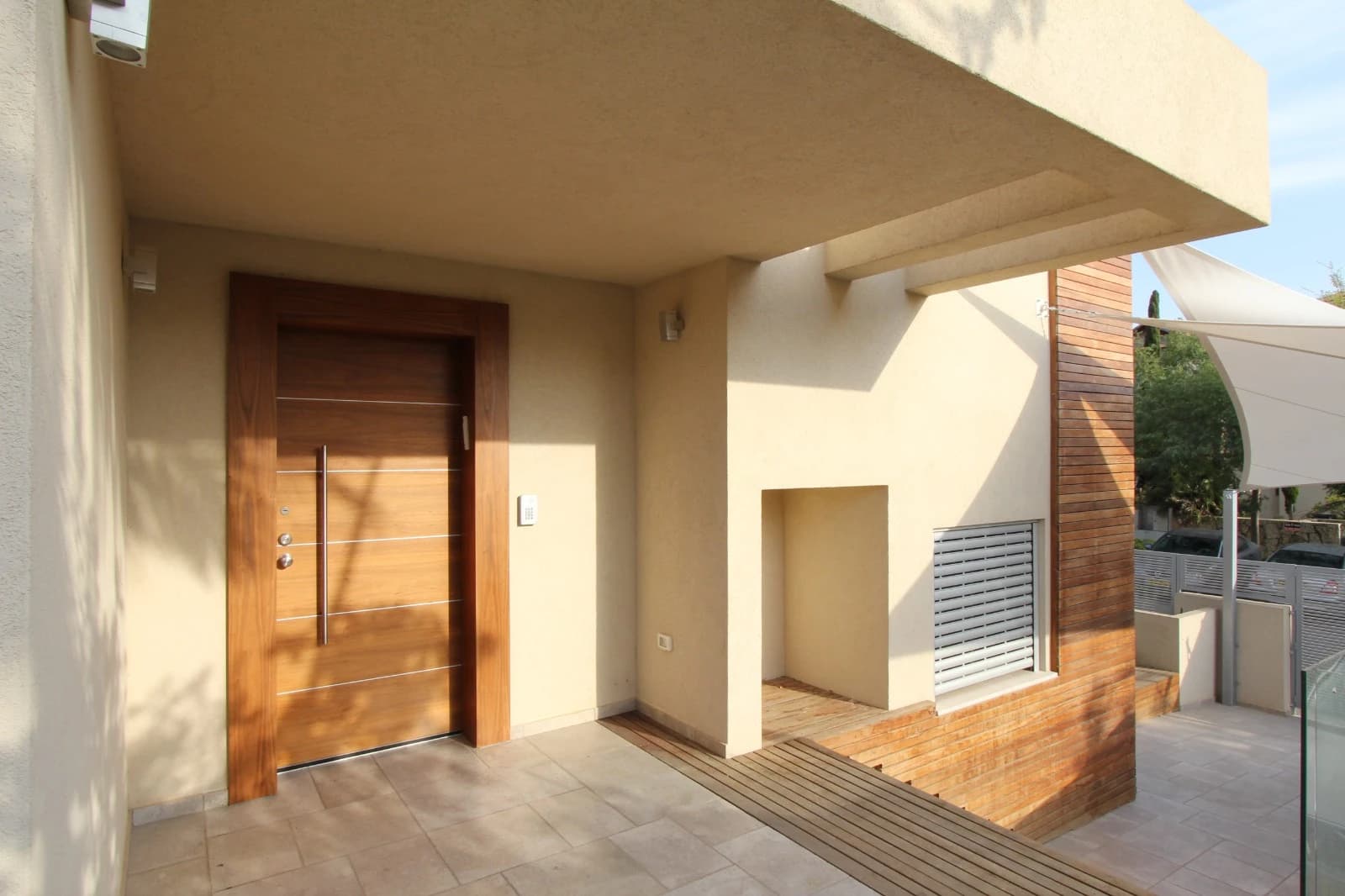 A timber entrance door with horizontal metal inlays, a long metal pull and a visible matching surround beneath a pale stucco canopy.